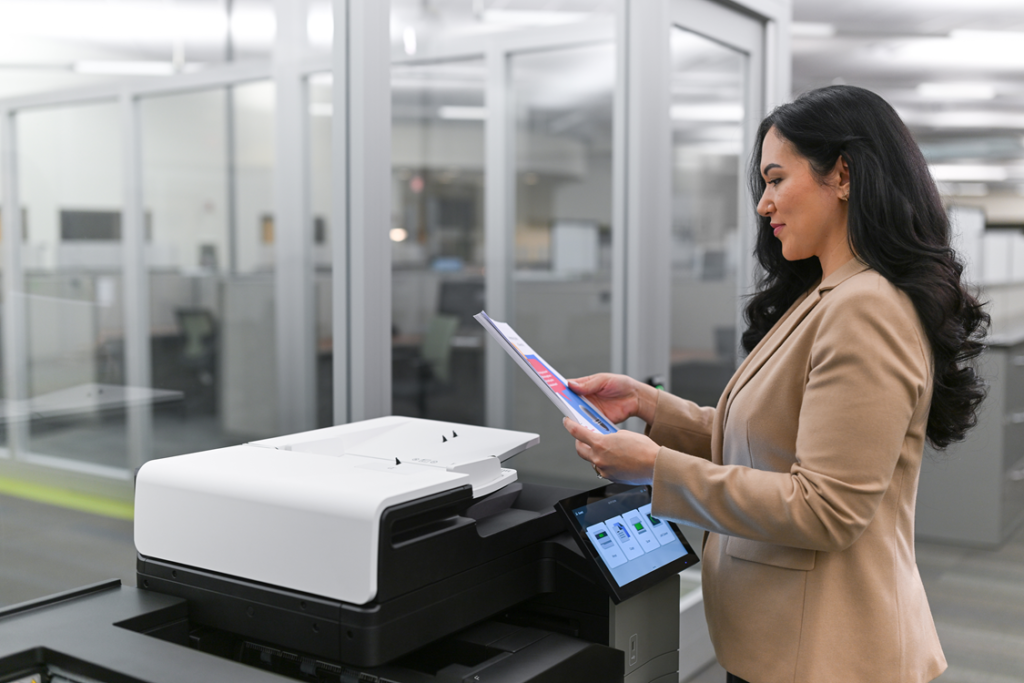Female colleague next to multifunction printer checking prints. 